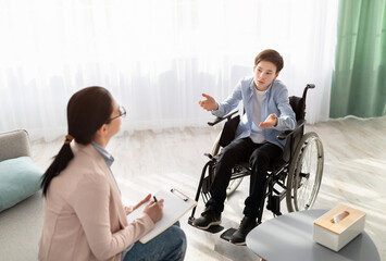 Female psychologist consulting disabled teenage boy in wheelchair at office