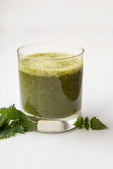 Glass of healthy nettle smoothie decorated with fresh nettle leaves. Nettle herb coctail on the white background.