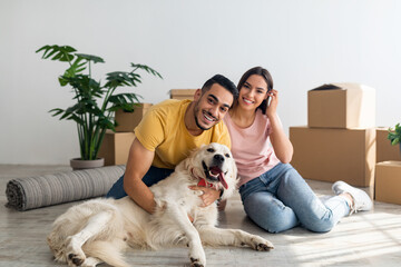 Full length portrait of happy young diverse couple with their dog posing on floor of new home on...
