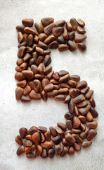 number five consists of large brown pine nuts on a background of gray marble created from natural...