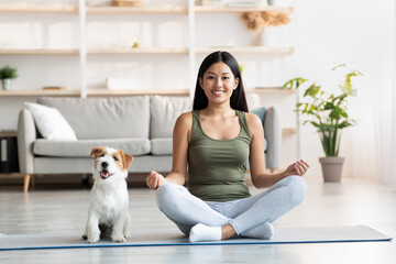 Positive young woman doing yoga with her dog at home - obrazy, fototapety, plakaty