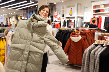 Photo of young attractive brunette woman with a short haircut in a white sweater chooses stylish and casual winter clothes in a store in a shopping centre