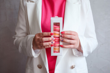 Close up of packaging of pink macaroons in woman's hands in front of her pink top and white jacket.