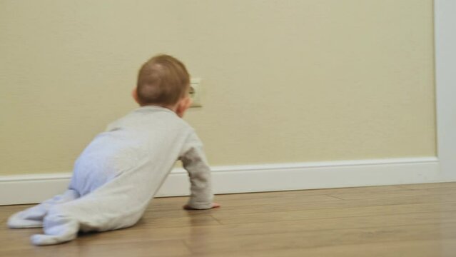 Baby toddler reaches into the electrical outlet on the home wall with his hand. Danger and protection of child fingers from electric shock