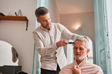 Middle aged son cutting hair to his retirement father by himself at home while chatting