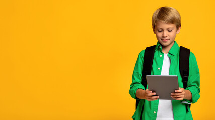 Smiling caucasian teen boy student with backpack typing on tablet and watching educational video