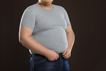 Overweight man trying to button up tight jeans on dark brown background, closeup