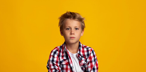 Serious seriously calm cute caucasian teenage boy looking at camera, isolated on yellow background
