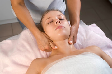 Fototapeta na wymiar Massage therapist is massaging head, shoulders and neck to woman in cosmetology clinic. Beautician making skincare and stimulation procedure. Spa treatment and massage in beauty salon.