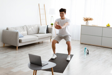 Asian guy doing squats exercise watching online tutorial