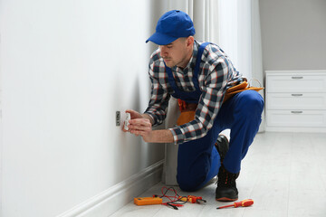 Professional male electrician repairing power socket in room - obrazy, fototapety, plakaty