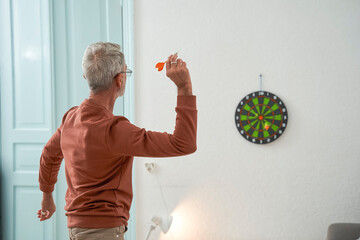 Grey haired mature man playing darts at home at his cozy room