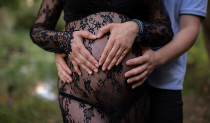 Pregnant Woman in Beautiful Clothes with her Husband on the Background of Foliage. Carrying the Gift of New Life.