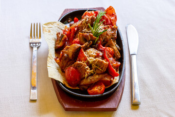 Traditional homemade stewed pork, beef, lamb or venison goulash with bell peppers, carrots and rosemary laid out on a pita in a frying pan on a wooden tray.