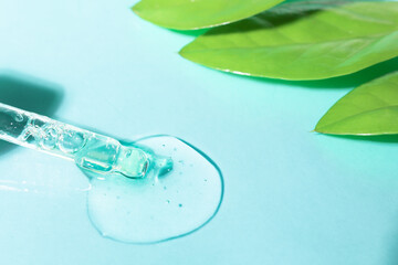Transparent cosmetic gel in a glass pipette on a colored background with green leaves of the plant....