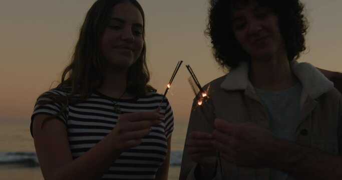 Friends playing happily with sparklers at seaside on sunset