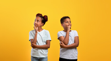 Pensive afro-american boy and girl posing on yellow studio background