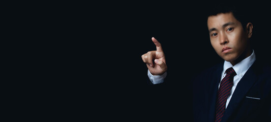 Businessman pointing to something or touching a touch screen on black background.