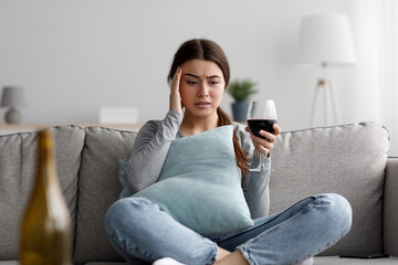 Obraz premium Sad depressed attractive millennial caucasian woman suffering from headache and drinking alcohol at home