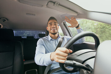 Cheerful middle-eastern guy driving auto, greeting someone