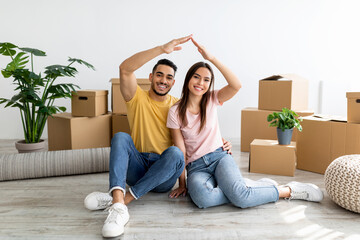 Full length of Arab man and his girlfriend making house gesture, sitting on floor among carton...