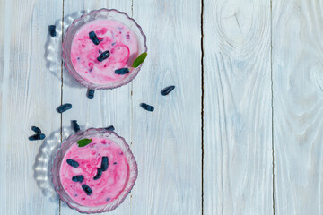 Berry yogurt with honeysuckle berries, purple milk yogurt with natural berries in spring on a white wooden table