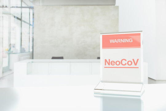 A plastic sign with the words Warning NeoCoV is standing on a table in front of the closed reception desk. 3D template on the theme of a new strain of coronavirus. Empty space for text or information