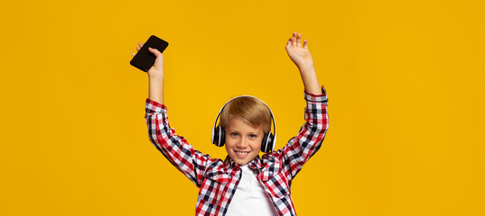 Emotional excited smiling caucasian teen boy in earphones with phone dancing and raising hands