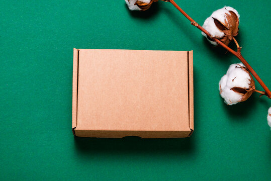 Brown cardboard box on green background with cotton flower