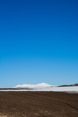 残雪の残る畑と雪山と青空　大雪山

