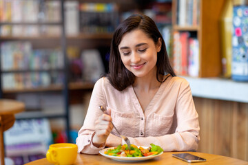 Pretty latin lady tasting fresh healthy salad, sitting at cafe or restaurant in daytime, enjoying delecious lunch