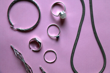 Arrangement of various silver jewelry accessories on pink background. Flat lay.