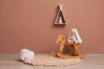 Rocking horse with bunny toy, wicker basket and wigwam shaped shelf on pink wall © New Africa