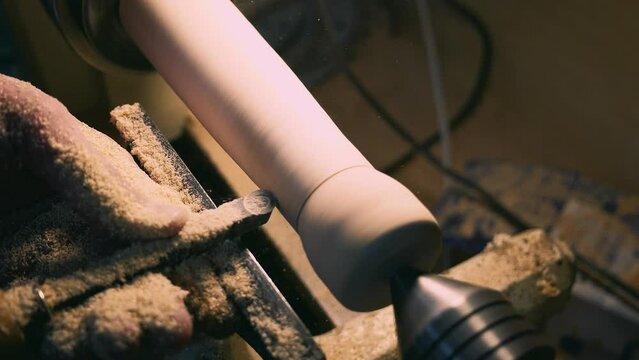 A worker cuts a piece of wood on a lathe with a woodworking tool