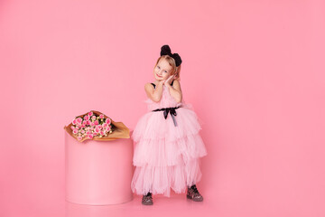 Child girl in a pink dress on a pink background, with a bouquet of roses, fashionable, stylish and...