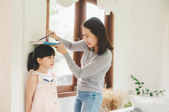 Asian Mother measuring height of her daughter near wall