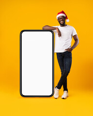 African Guy Standing Near Cellphone Screen Wearing Santa Hat, Studio