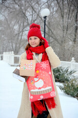 Winter shopping. A young woman in a red scarf and hat stands with gift bags on the street in winter.