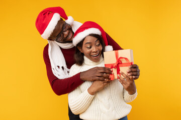 African American Husband Surprising Wife Giving Christmas Gift, Yellow Background