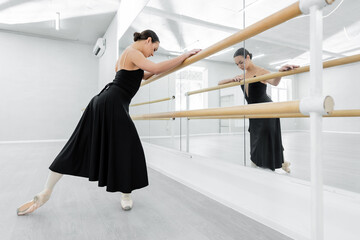 young ballerina in black dress training at barre near mirrors