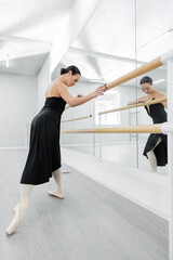 Fototapeta na wymiar ballet dancer in black dress exercising at barre near mirrors