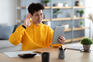 Smiling asian man holding digital tablet waving hand