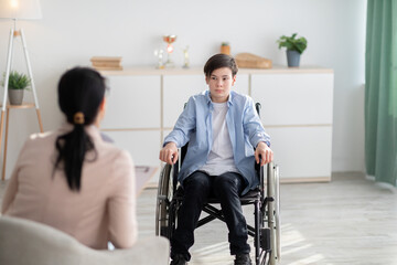 Psychological help service. Disabled teen boy in wheelchair having psychotherapy session with counselor at clinic