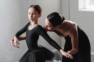 young ballet teacher assisting girl in black tutu during dance lesson