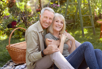 Fototapeta premium Portrait of senior couple sitting in garden and hugging, having picnic outdoors and smiling to camera