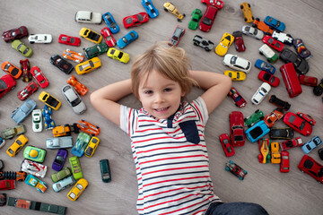 Cute toddler child, blond boy, playing with colofrul cars, different sizes and colors on the floor