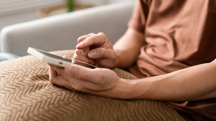 Technology Concept The man sitting next to a pot of plant, putting a small pillow on his lap, and checking something on his smartphone