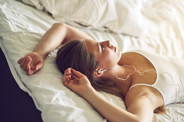 Musical mornings. Shot of a young woman listening to music while relaxing on her bed.