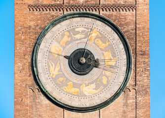 Fototapeta na wymiar A huge unusual dial of an old clock with horoscope signs on a brick tower against the blue sky