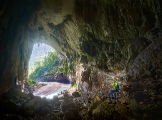 Womam traveler explores an incredible exit from one of largest natural caves in world from high rocky hill. - 483089982